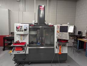 A CNC milling machine with a control panel and storage shelves in an industrial workshop setting.