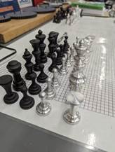 Close-up of a chessboard with black and silver chess pieces set up in starting positions.