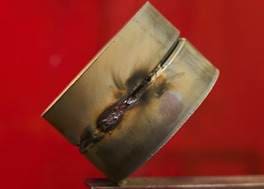 A distorted, damaged gold ring with a prominent crack and burn marks, set against a solid red background.