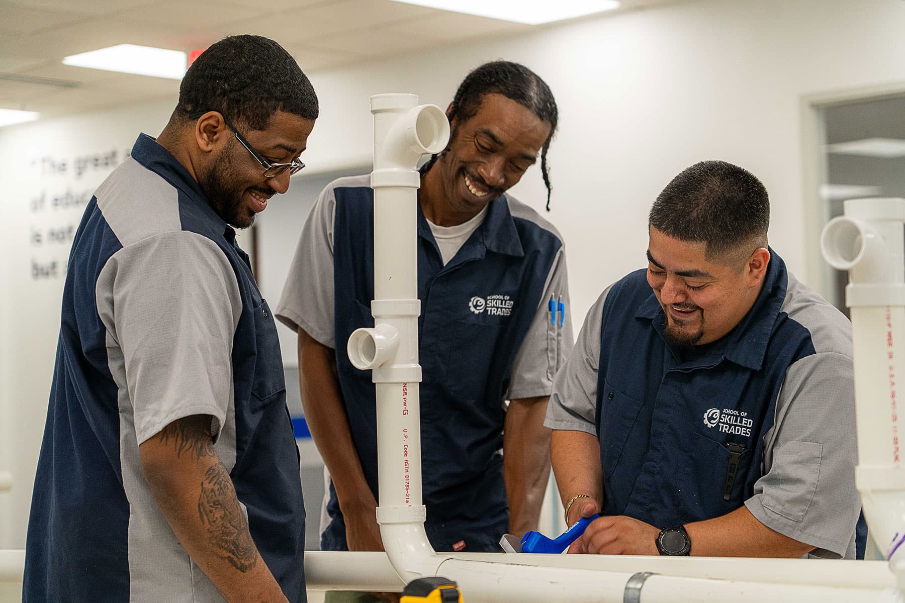 Three men in matching uniforms work together on assembling PVC pipes indoors, appearing focused and collaborative.