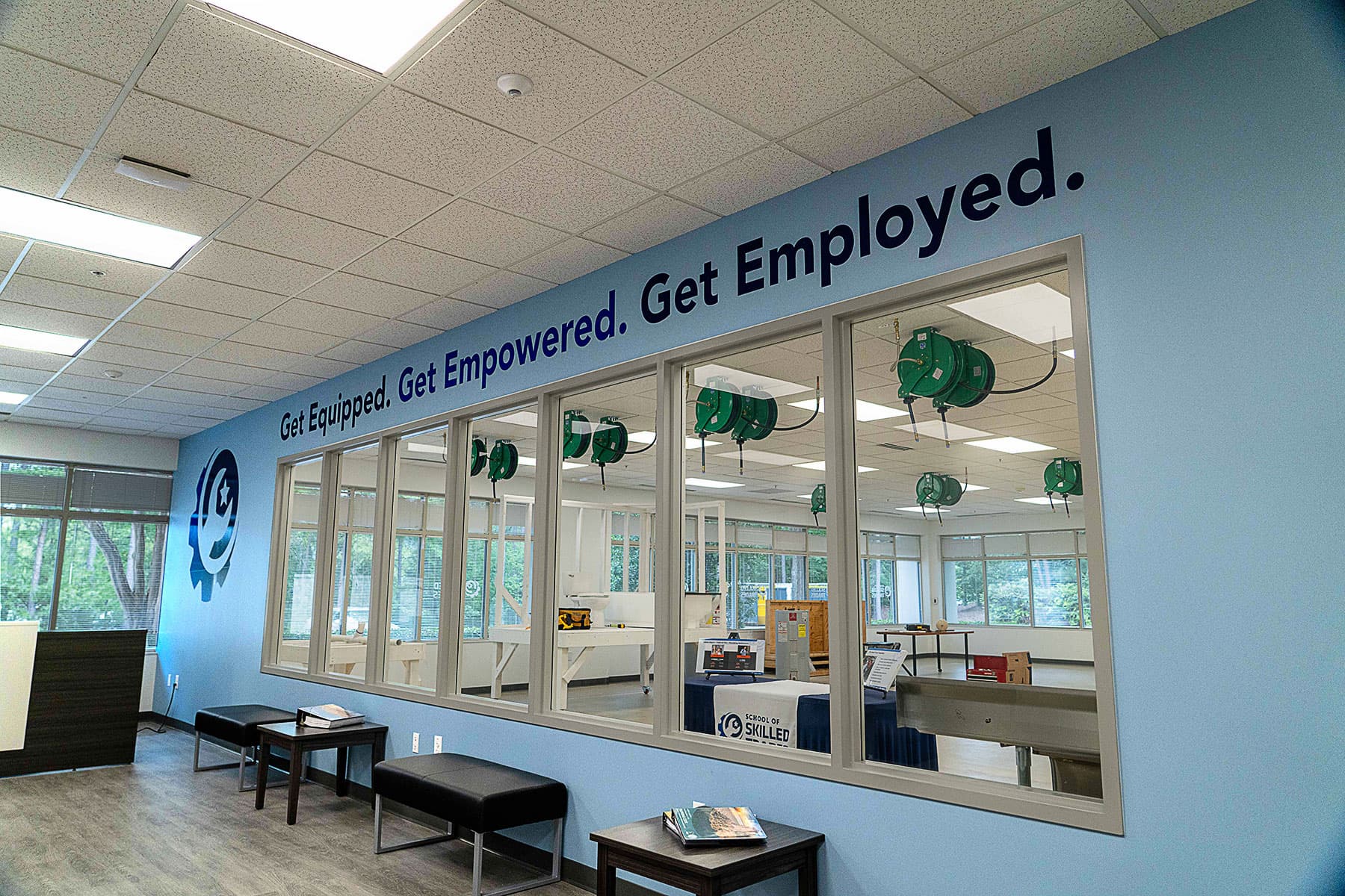 Interior view of a training center with blue walls, large windows, benches, and the slogan "Get Equipped. Get Empowered. Get Employed." displayed above the windows.